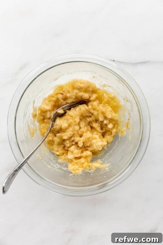 Mashed bananas with a fork in a clear mixing bowl, showing the creamy texture.
