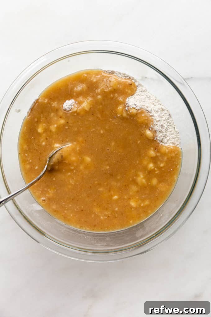 Wet and dry banana bread batter in a clear mixing bowl, showing the moment of combining.