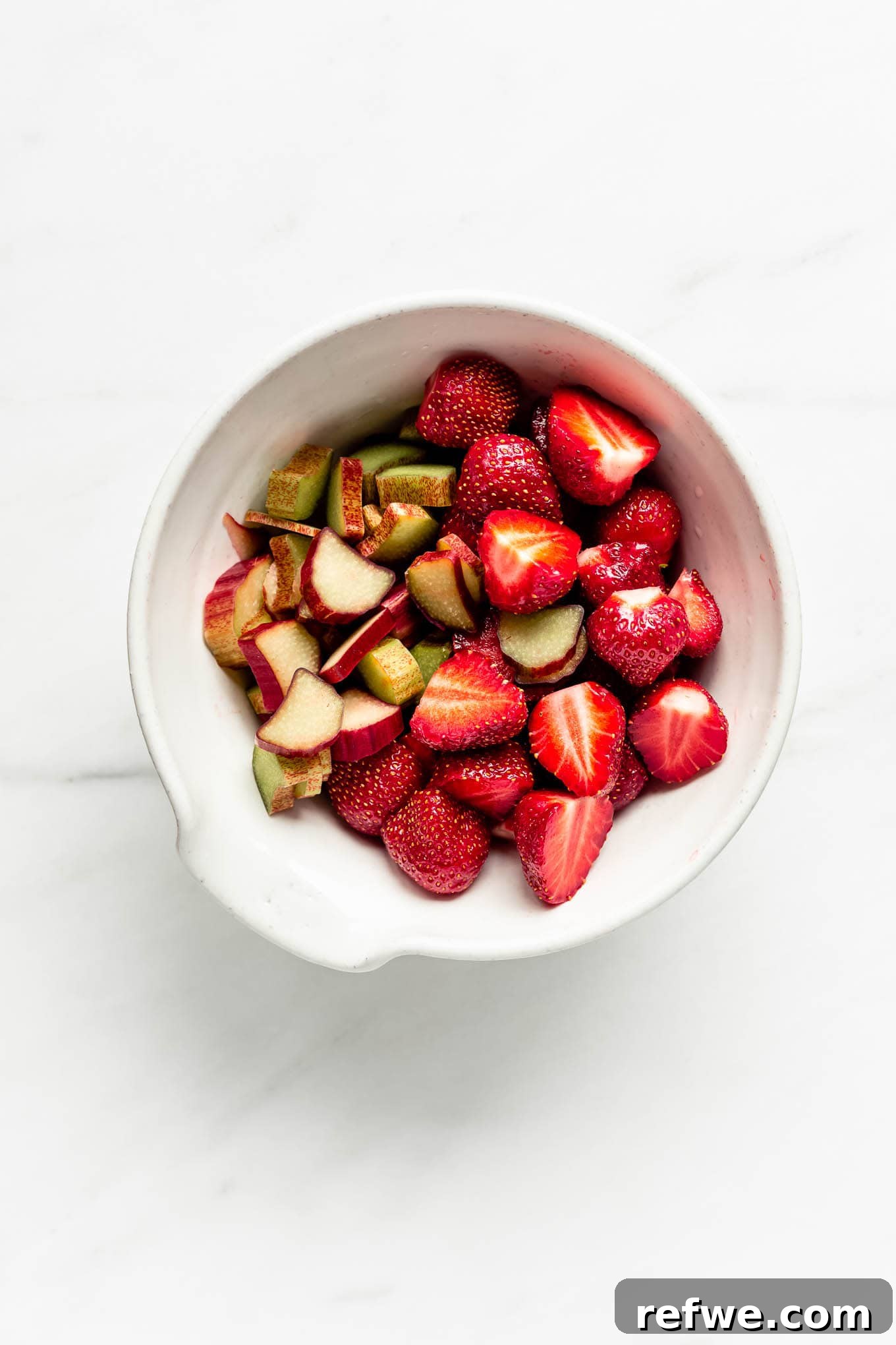 Freshly cut strawberries and rhubarb pieces tossed together in a large mixing bowl, ready for the crisp.