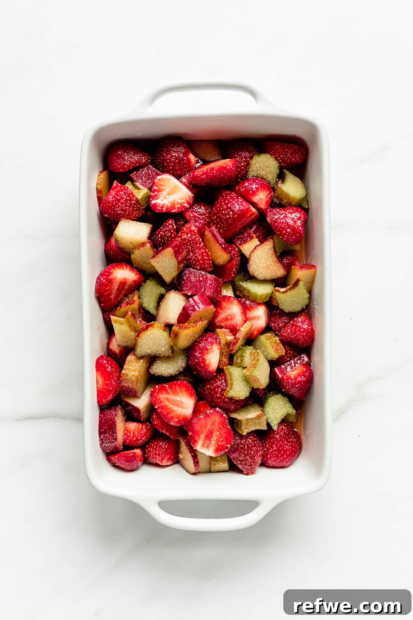 The vibrant strawberry and rhubarb fruit mixture spread evenly in a white ceramic baking dish, ready for the topping.