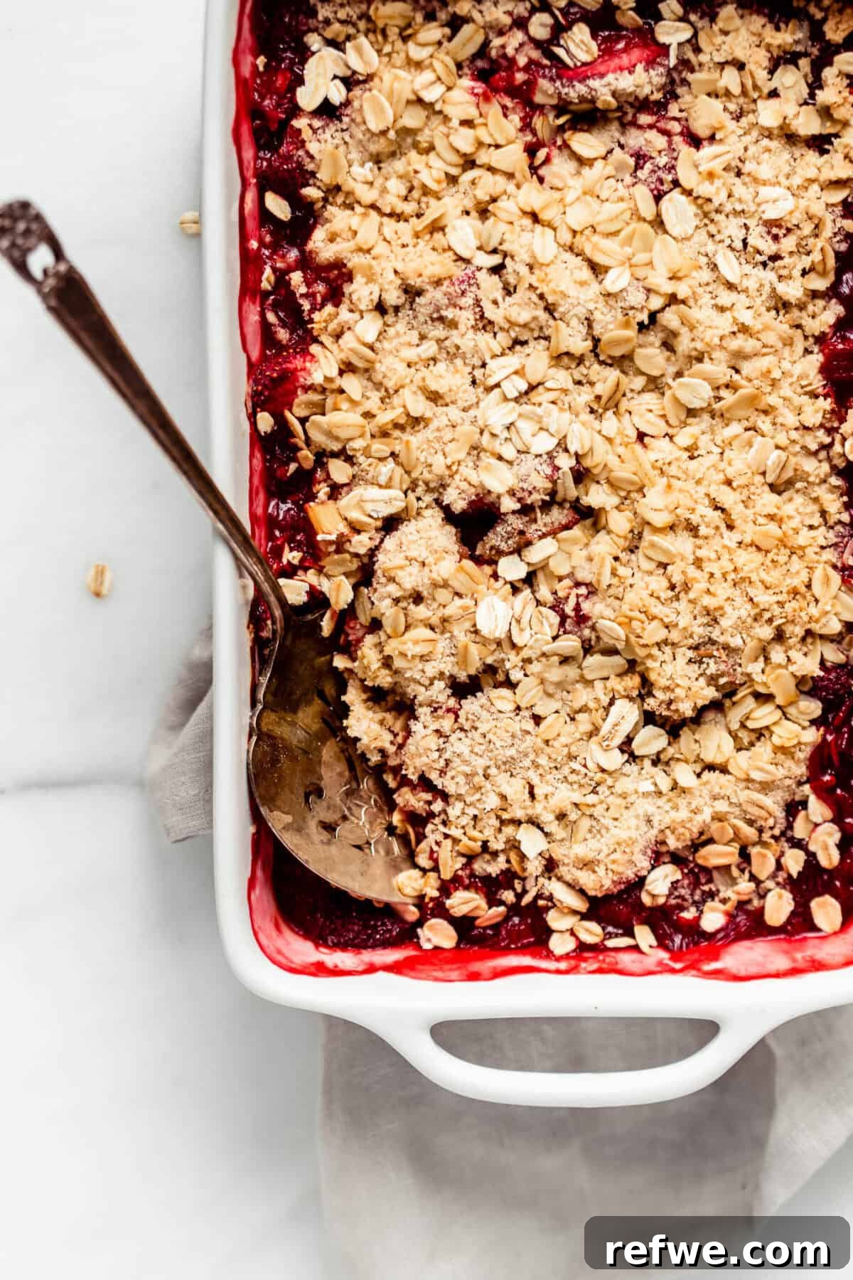 A perfectly baked healthy strawberry rhubarb crisp, golden brown and bubbly, cooling in a white ceramic baking dish.