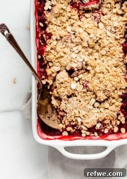 A baked healthy strawberry rhubarb crisp with a spoon, ready to be served.