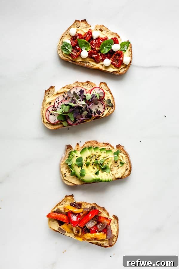 Effortless Hummus Toast Explorations 2 Four vibrant pieces of hummus toast with various colorful vegetable toppings, including tomatoes, radishes, avocado, and roasted peppers, beautifully arranged on an elegant marble serving board, ready to be enjoyed.