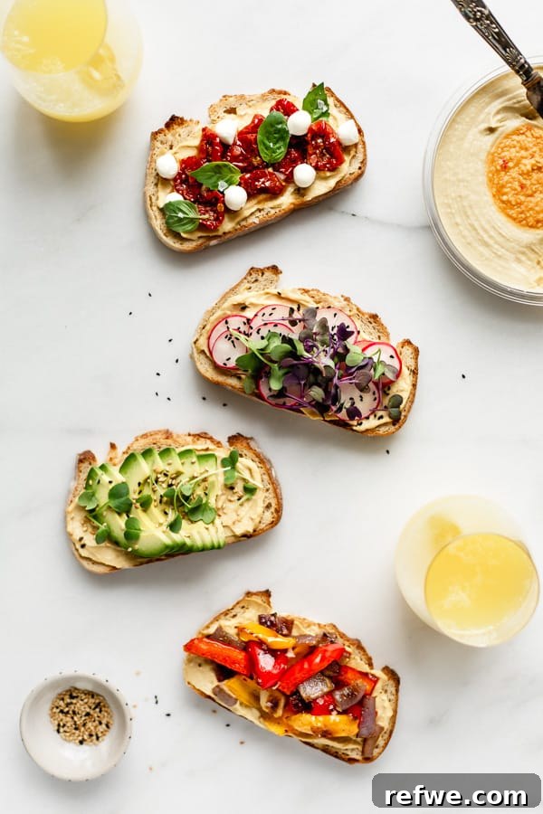 Effortless Hummus Toast Explorations 3 A charming scene featuring four different hummus toasts adorned with diverse toppings, gracefully presented alongside two sparkling glasses of mimosas and a fresh container of Sabra hummus, perfect for a delectable brunch gathering.