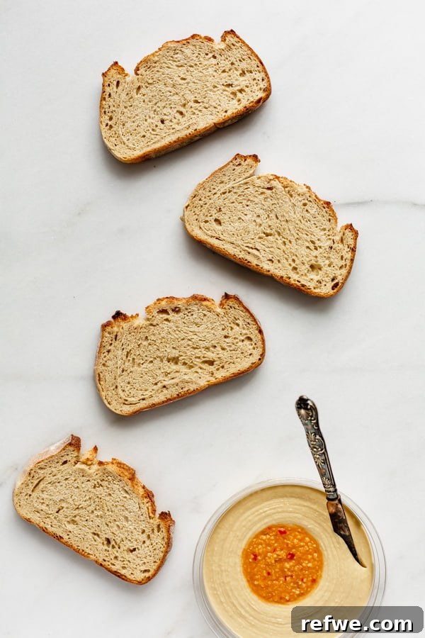 Effortless Hummus Toast Explorations 4 Four pieces of freshly toasted bread laid out neatly with a container of creamy hummus on the side, accompanied by various fresh ingredients in small bowls, all ready for the next step of assembly.