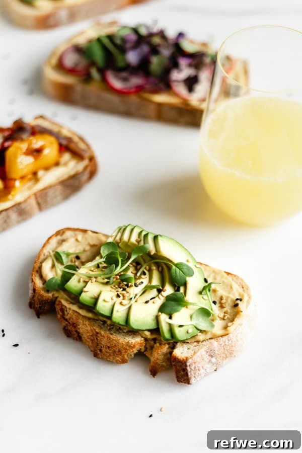 Effortless Hummus Toast Explorations 7 A single piece of delectable hummus toast generously topped with fresh, vibrant avocado slices, sprinkled with sesame seeds and a pinch of salt, beautifully resting on a pristine marble surface.