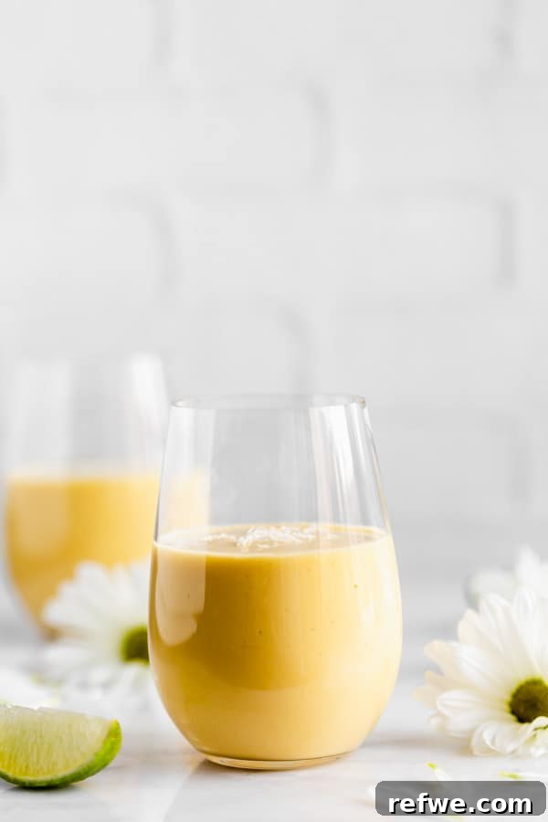 a glass of vegan mango lassi with flowers in the background