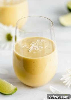 a glass of vegan mango lassi on a marble board with limes and flowers
