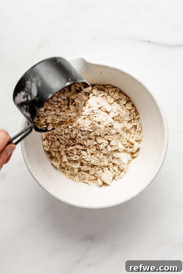 Golden Raspberry Crumble Bars 3 Pouring oats into a mixing bowl with almond flour and cinnamon, ready for the next step of making crumble dough.
