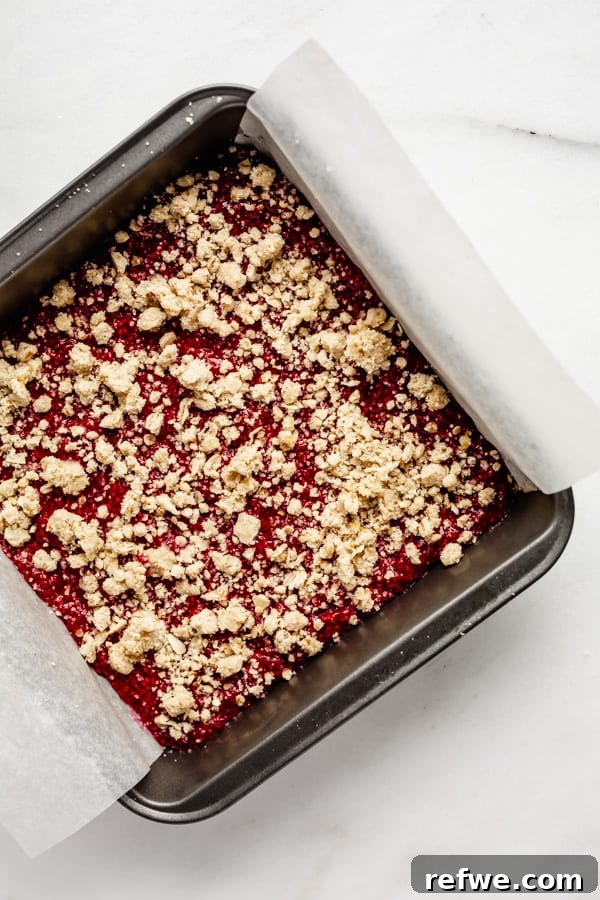 Golden Raspberry Crumble Bars 7 Unbaked raspberry crumble bars in a pan, topped with the remaining crumble mixture, ready for the final bake.