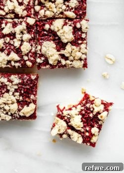 A close-up of a raspberry crumble bar with a bite taken out of it, showcasing the layers of crumbly crust and fruit filling.
