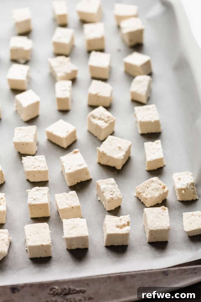 Peanut Tofu Power Bowls 4 Tofu cubes evenly scattered on a parchment-lined baking sheet, ready for baking to achieve perfect crispiness.