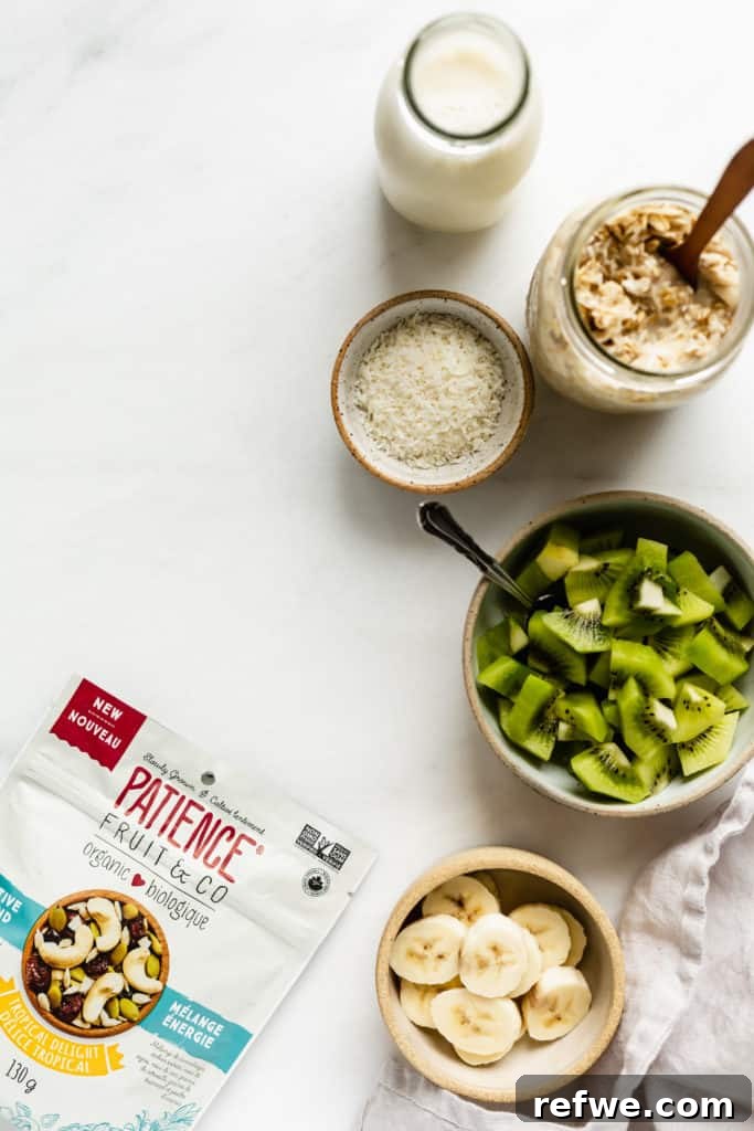 Tropical Coconut Cashew Bircher 3 A flat lay photograph showcasing the key ingredients for Bircher Muesli: almond milk, shredded coconut, rolled oats, fresh kiwi slices, and banana chunks, neatly arranged on a light background.