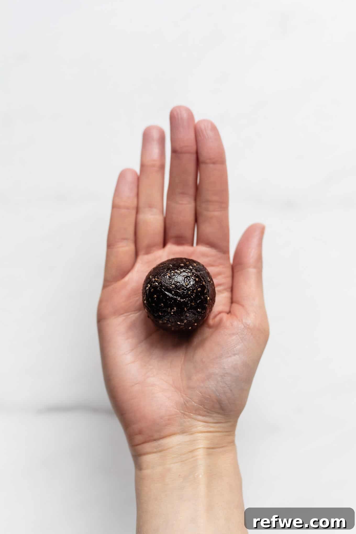 Fudgy Date & Chocolate Bites 6 A perfectly rolled chocolate date ball held in a hand, showing its smooth, round shape.