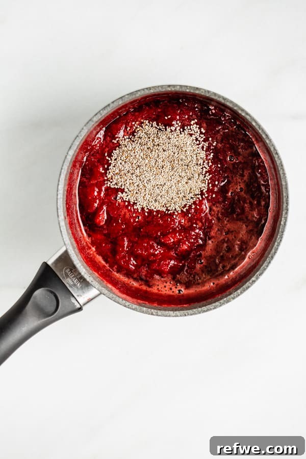 Homemade Chia Seed Jam Made Easy 3 A pot filled with chopped strawberries, lemon juice, and maple syrup simmering gently on a stovetop, ready for chia seeds.