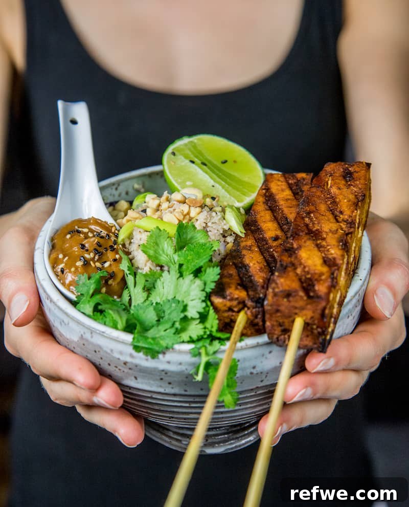 Flavorful Tofu Satay and Cauliflower Fried Rice 3 Close-up of Tofu Satay skewers drizzled with peanut sauce, beside a bowl of cauliflower fried rice