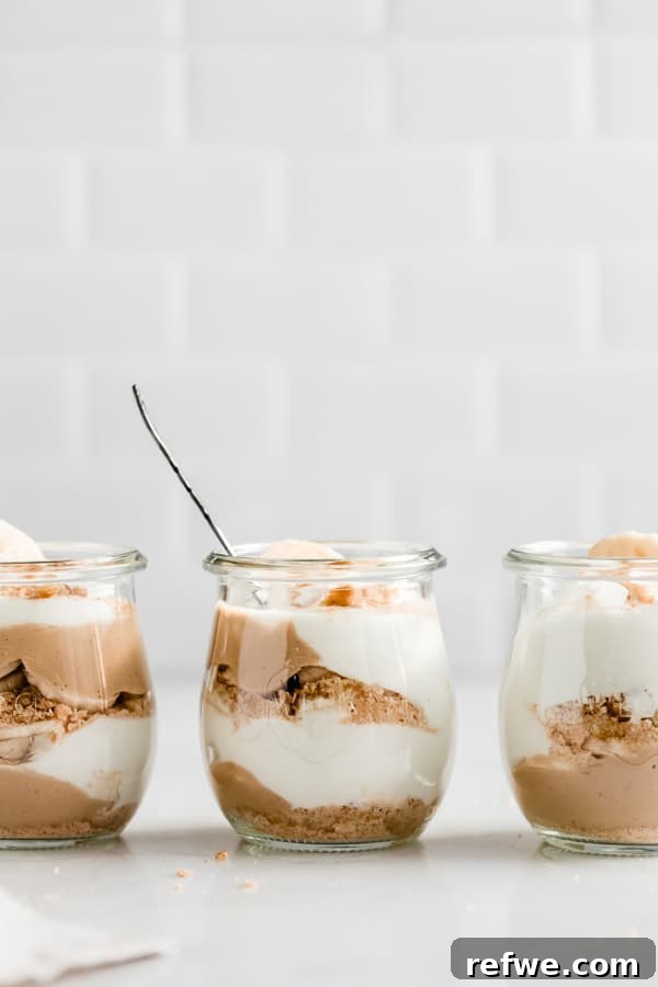 Three elegant cups of vegan banana cream pie parfaits neatly lined up, beautifully displaying the distinct layers of cream, pudding, and fresh bananas within each glass