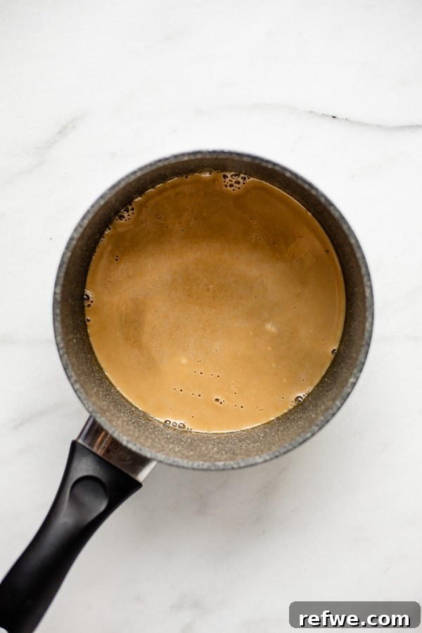 A grey pot containing a bubbling vegan caramel mixture, illustrating the initial stage of creating the homemade vanilla pudding base
