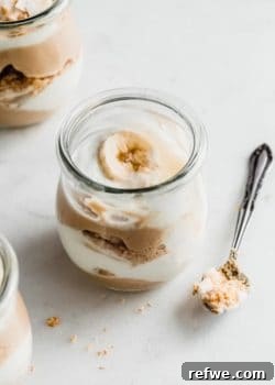 A close-up of a vegan banana cream pie parfait in a glass, with a spoon nearby, highlighting the luscious layers and inviting texture