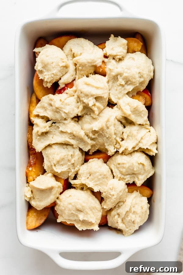 Luscious Gluten-Free Peach Cobbler 4 An unbaked gluten-free peach cobbler in a white baking dish, topped with dollops of biscuit dough over the peach filling.