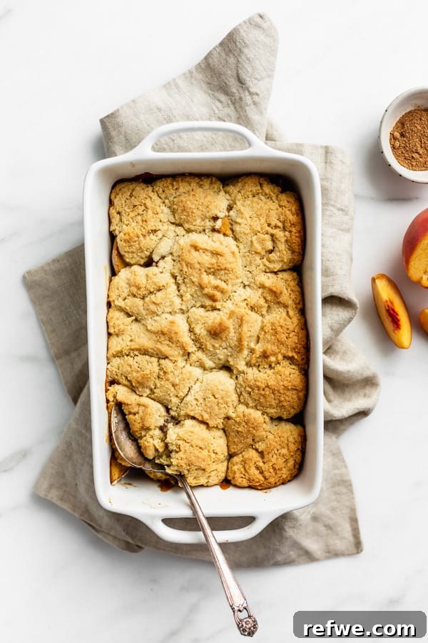 Luscious Gluten-Free Peach Cobbler 5 A freshly baked gluten-free peach cobbler, golden brown and bubbly, presented in a white baking dish on a beige linen napkin.
