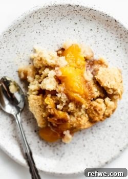 A slice of gluten-free peach cobbler on a white speckled plate, highlighting its delicious topping.