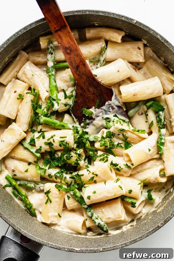 Bright Lemon Asparagus Pasta 5 A large pot filled with rigatoni noodles, mixed with bright green asparagus pieces and fresh parsley, all coated in a rich, creamy sauce.