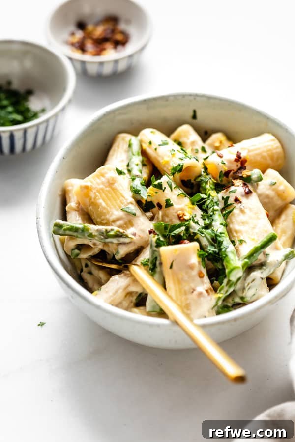 Bright Lemon Asparagus Pasta 6 A close-up shot of creamy rigatoni pasta, beautifully plated in a white bowl, with a gold fork resting in it, highlighting the smooth sauce and tender asparagus.