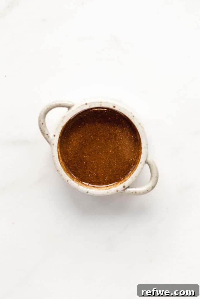 A small bowl holding a rich, amber-colored Singapore noodle sauce, ready to be incorporated into the dish.