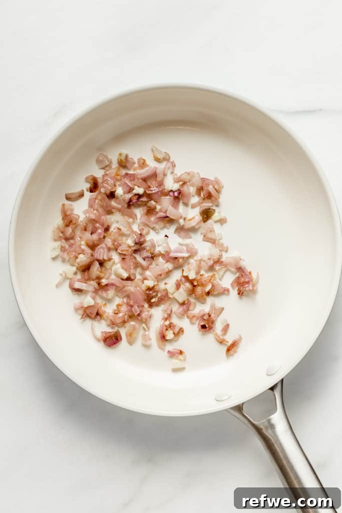 Finely chopped shallots and garlic sizzling in a white pan, becoming fragrant and translucent.