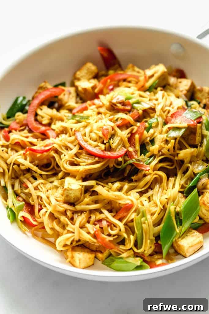 A wider shot of vibrant Singapore noodles in a pan, showcasing colorful peppers and savory tofu amidst the noodles.
