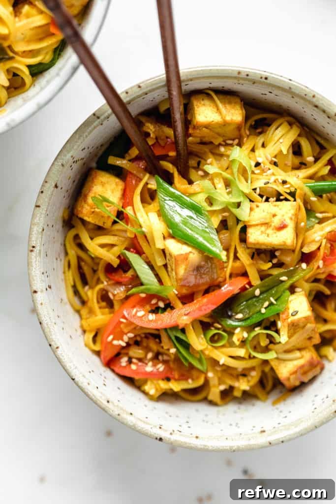 A vibrant bowl of Vegan Singapore Noodles, elegantly garnished with fresh sliced green onions and toasted sesame seeds, ready to be enjoyed.