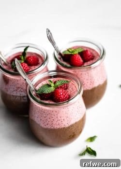 Three cups of chocolate and raspberry chia pudding topped with raspberries and fresh mint, ready to serve.