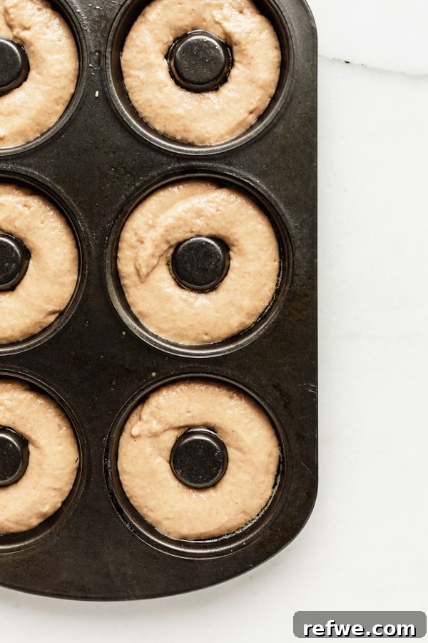 Warm Cinnamon Vegan Apple Cider Donuts 7 An unbaked donut batter filling the cavities of a donut pan, ready for the oven.