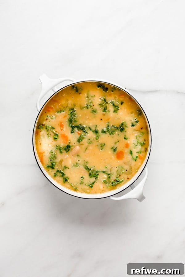 A white pot filled with a rich, creamy Tuscan white bean soup, some portions blended for smoothness.