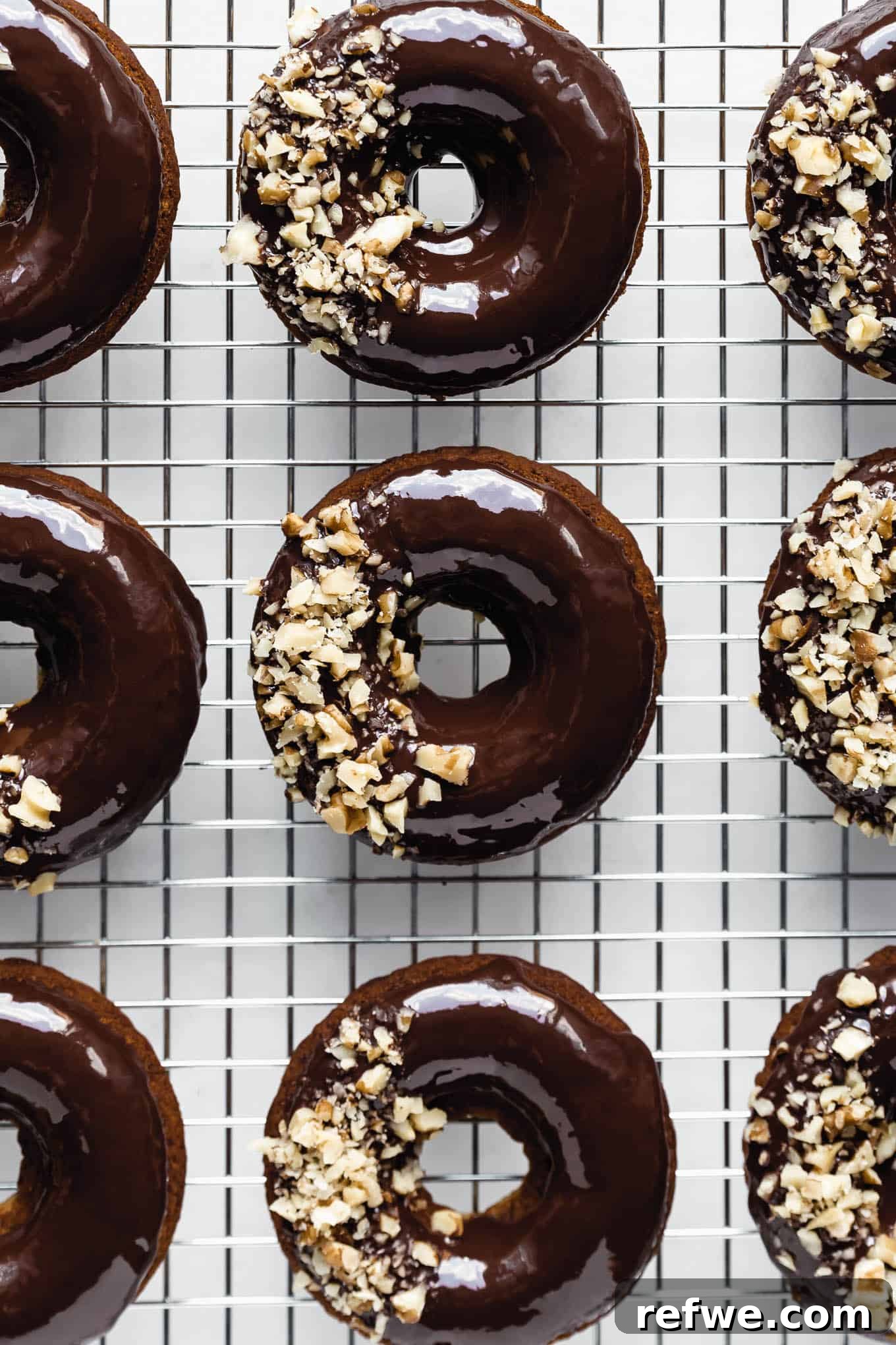 Soft Baked Vegan Banana Bread Donuts 2 Delicious baked vegan banana bread donuts topped with chocolate ganache and crushed walnuts, resting on a cooling rack.