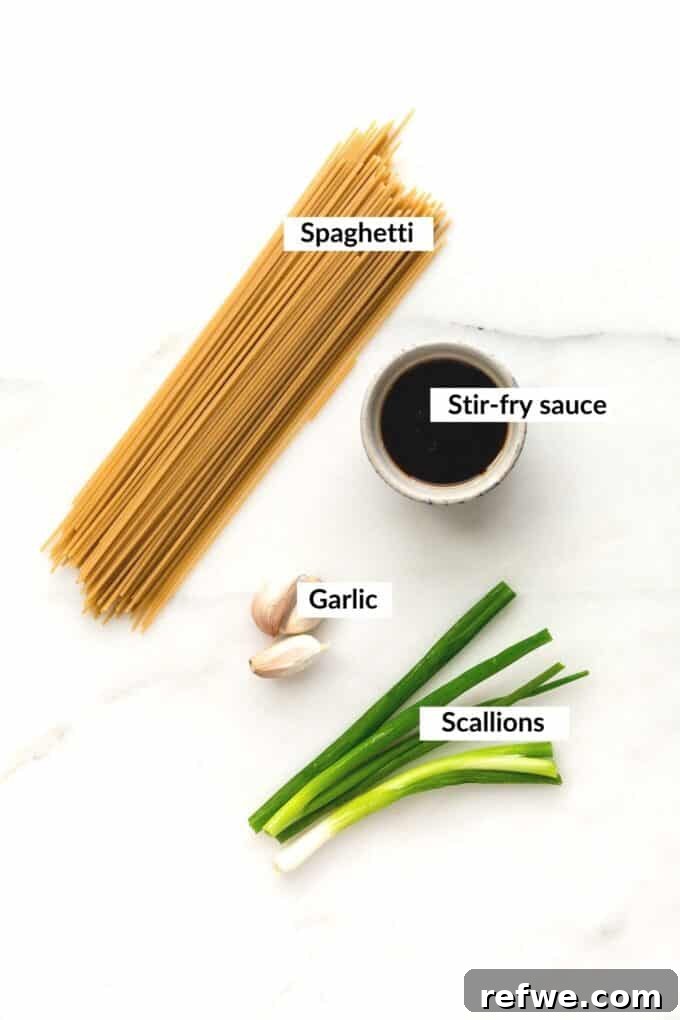 A collection of fresh ingredients laid out, including noodles, garlic cloves, scallions, and bottles of soy sauce, sesame oil, and sriracha.