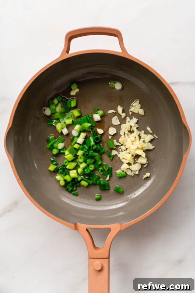 Finely chopped scallions and garlic sizzling in a vibrant pink pan.