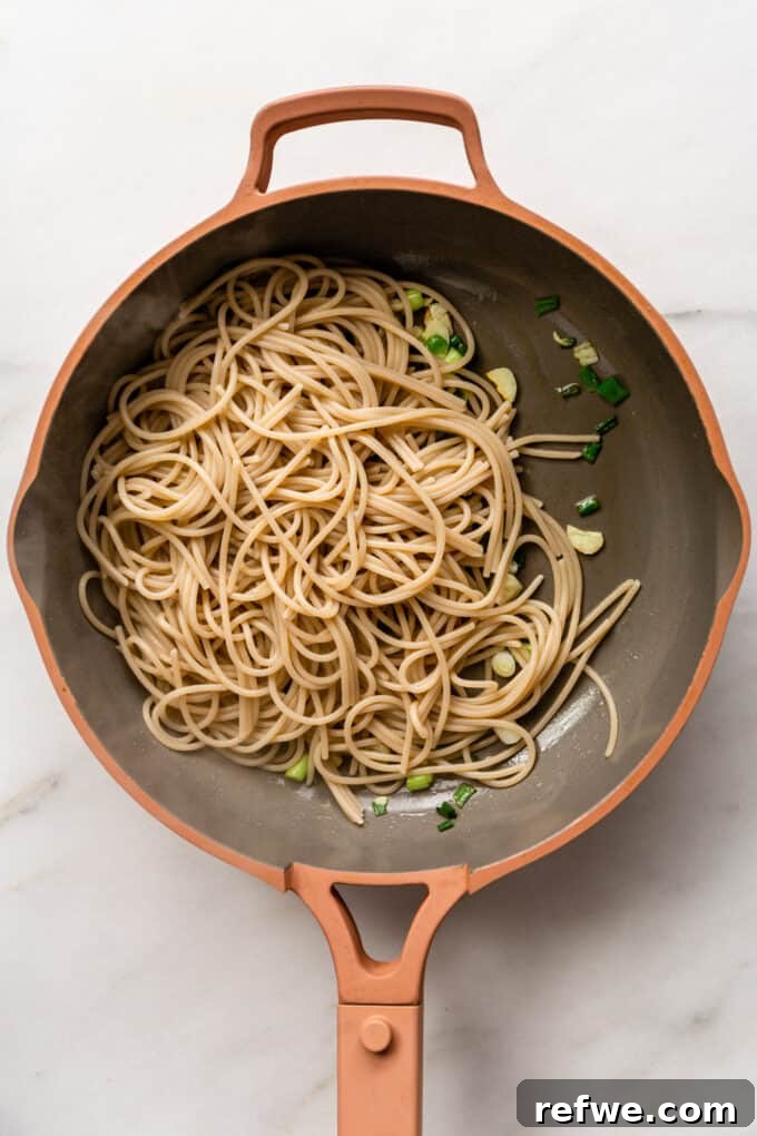 Cooked spaghetti, fresh scallions, and fragrant garlic expertly combined in a pink pan.