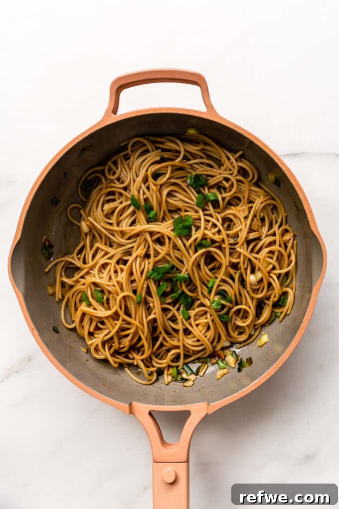 A pink pan filled with perfectly coated and glistening garlic noodles.