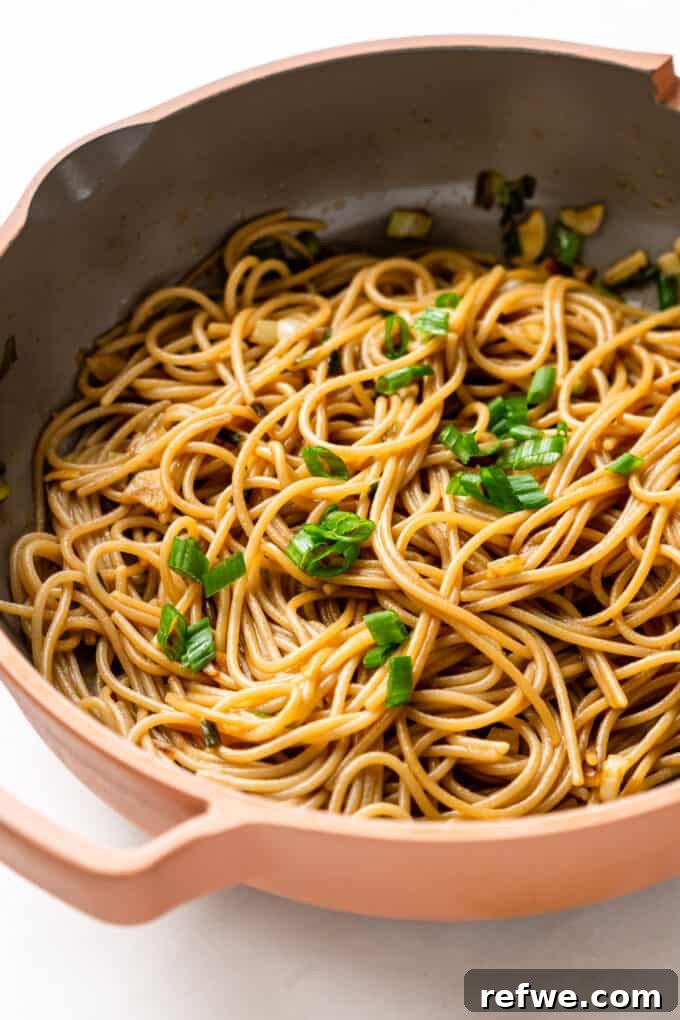 Garlic noodles in a pink pan, beautifully topped with freshly chopped scallions.