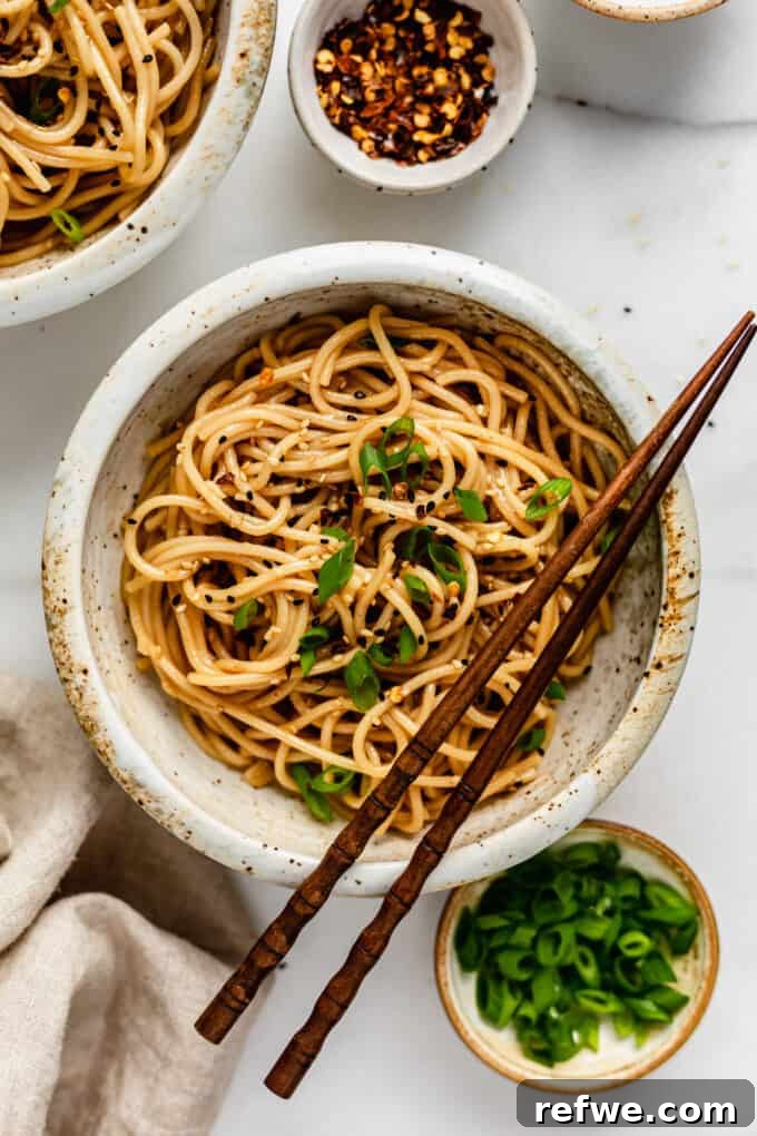 A perfectly plated bowl of garlic noodles, accompanied by small bowls of green onions and crushed red peppers for garnish.