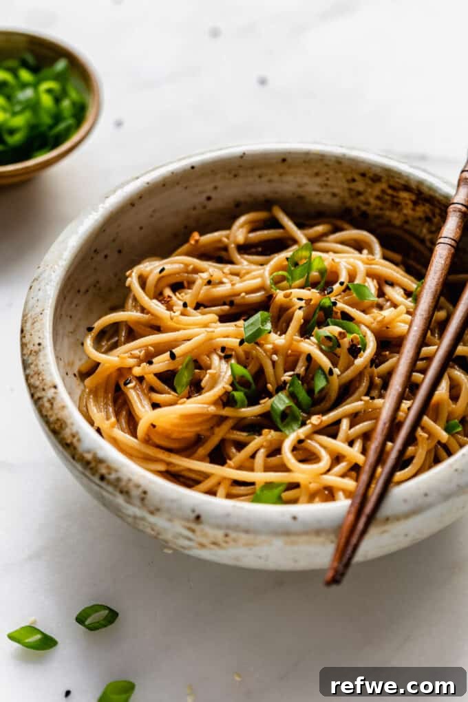 A beautifully presented bowl of garlic noodles, generously topped with vibrant green onions.