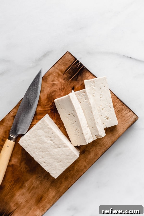 A block of extra-firm tofu expertly sliced into uniform, thick pieces on a rustic wooden cutting board, ready for various culinary preparations.