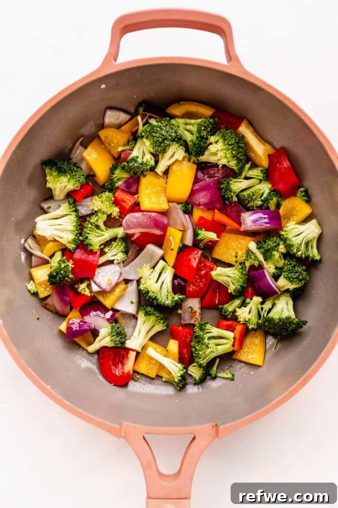 Fresh broccoli florets, sliced bell peppers, and chopped onions sautéing in a pan.
