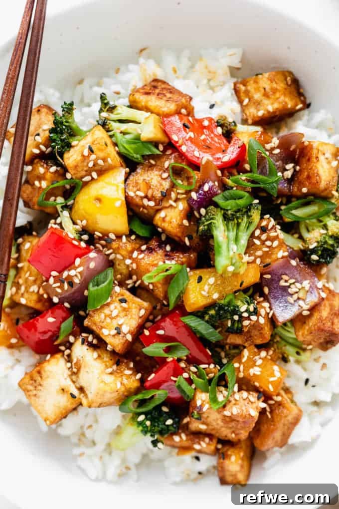 A vibrant bowl of crispy tofu stir fry with broccoli and bell peppers, generously topped with toasted sesame seeds and fresh herbs, ready to be enjoyed.