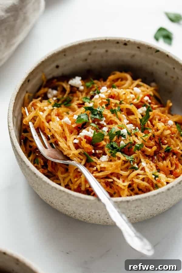 Golden Spaghetti Squash with Tangy Sun-Dried Tomatoes and Sweet Caramelized Onions 6 A close-up of a serving of sun-dried tomato spaghetti squash with goat cheese and parsley in a ceramic bowl.