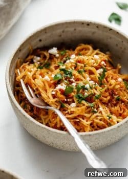 A close up of sun dried tomato spaghetti squash in a ceramic bowl, garnished with parsley.