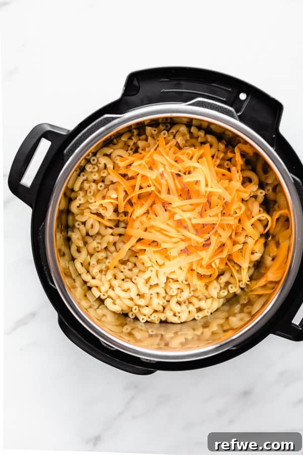 Quick Creamy Instant Pot Mac and Cheese 6 macaroni in an instant pot with a pile of orange shredded cheese on it