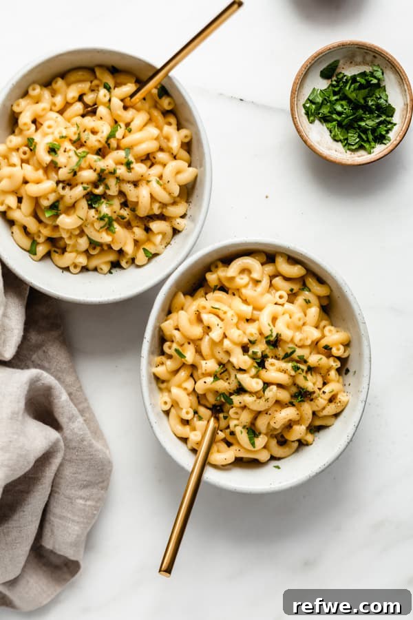 Quick Creamy Instant Pot Mac and Cheese 9 two bowls of mac and cheese on a marble board with a small bowl of parsley on the side
